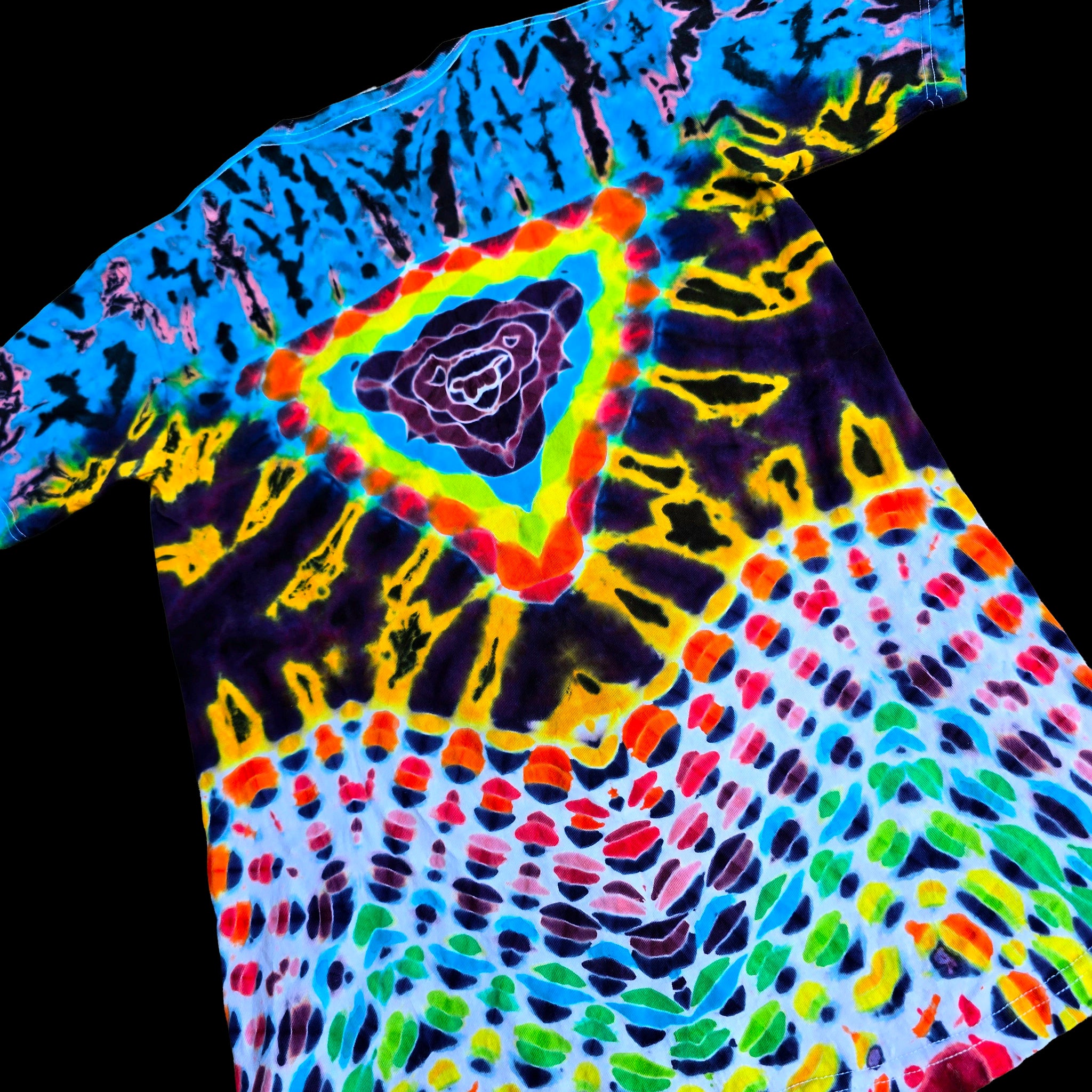 A short-sleeve tie-dye T-shirt laid flat on a black background, featuring a complex neon rainbow pattern with concentric triangles and splatter motifs in blue, yellow, green, red, orange, and purple.