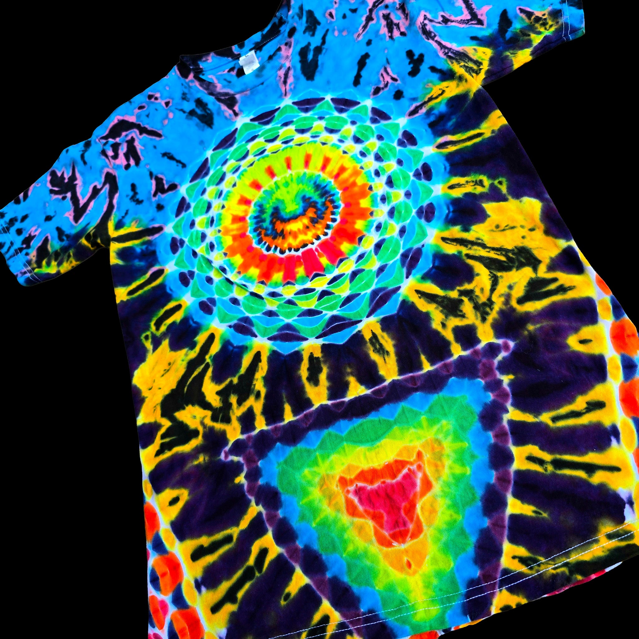 A short-sleeve tie-dye T-shirt laid flat on a black background, featuring a large spiral mandala design on the chest and a triangular rainbow motif near the lower right front.