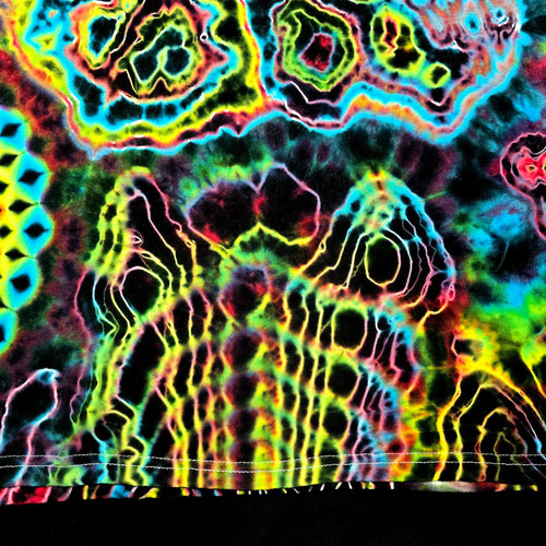 A close-up of a highly saturated tie-dye or psychedelic pattern with neon yellow, green, blue, pink, and purple outlines over a dark base. The fabric or material fills almost the entire frame, with a small black band visible along the bottom edge.