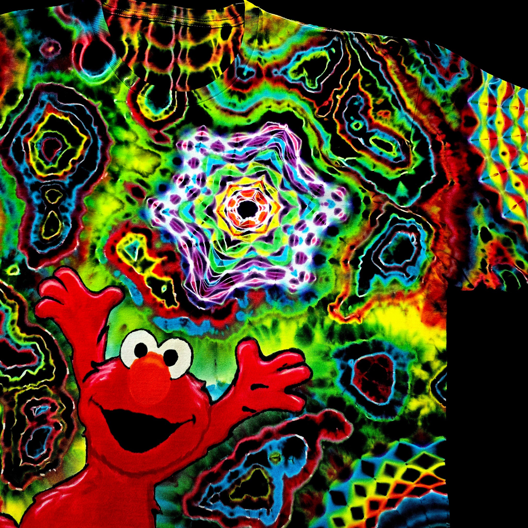 A close-up of a highly colorful tie-dye shirt featuring a red cartoon character with raised hands and a psychedelic kaleidoscopic pattern in neon green, blue, yellow, purple, and red.