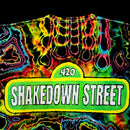 A close-up of a neon tie-dye t-shirt featuring a green street-sign style graphic that reads '420 SHAKEDOWN STREET' in white letters, set against a black background.