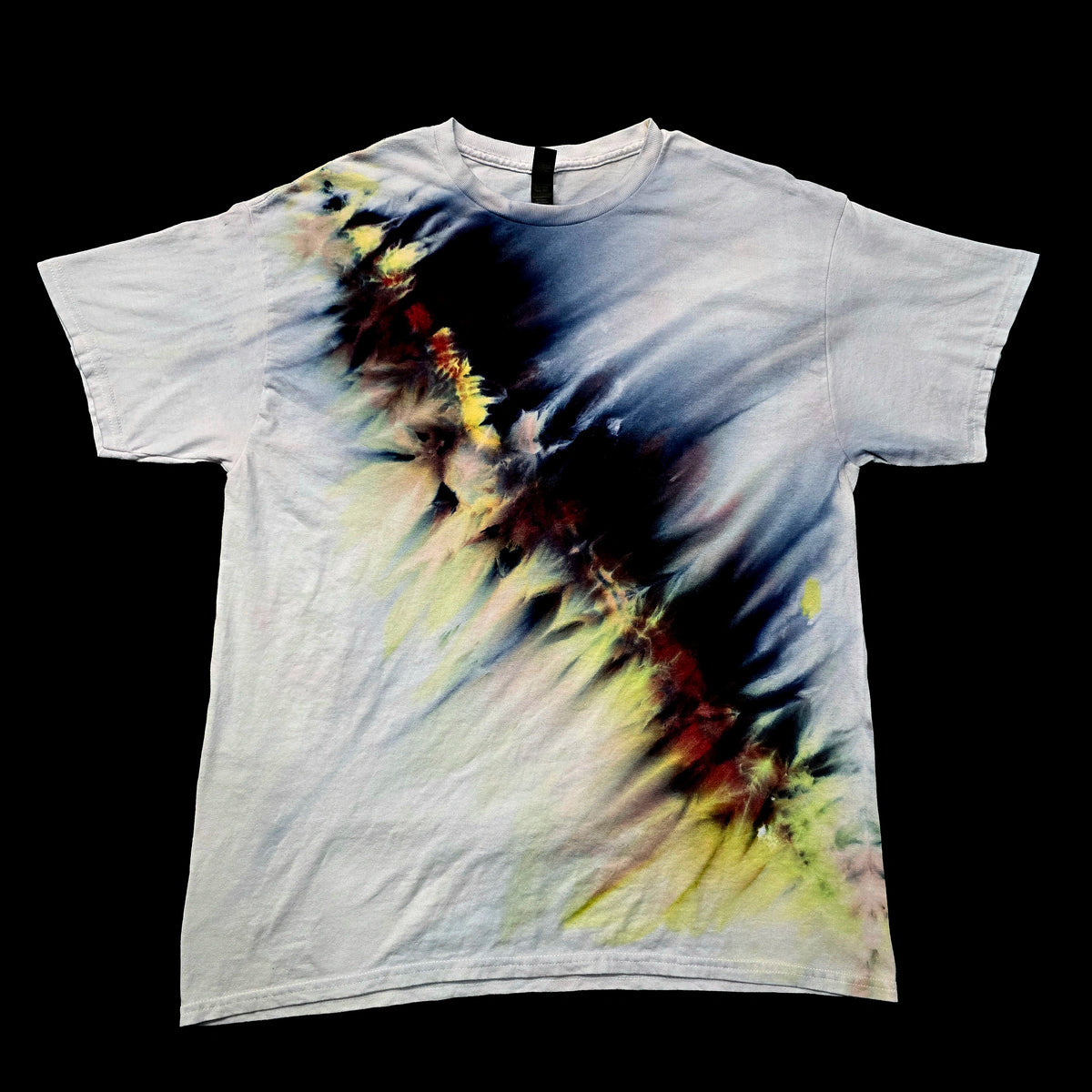 A white short-sleeve crewneck t-shirt featuring an abstract, painterly graphic print in black, blue, yellow, and red tones, laid flat against a solid black background.