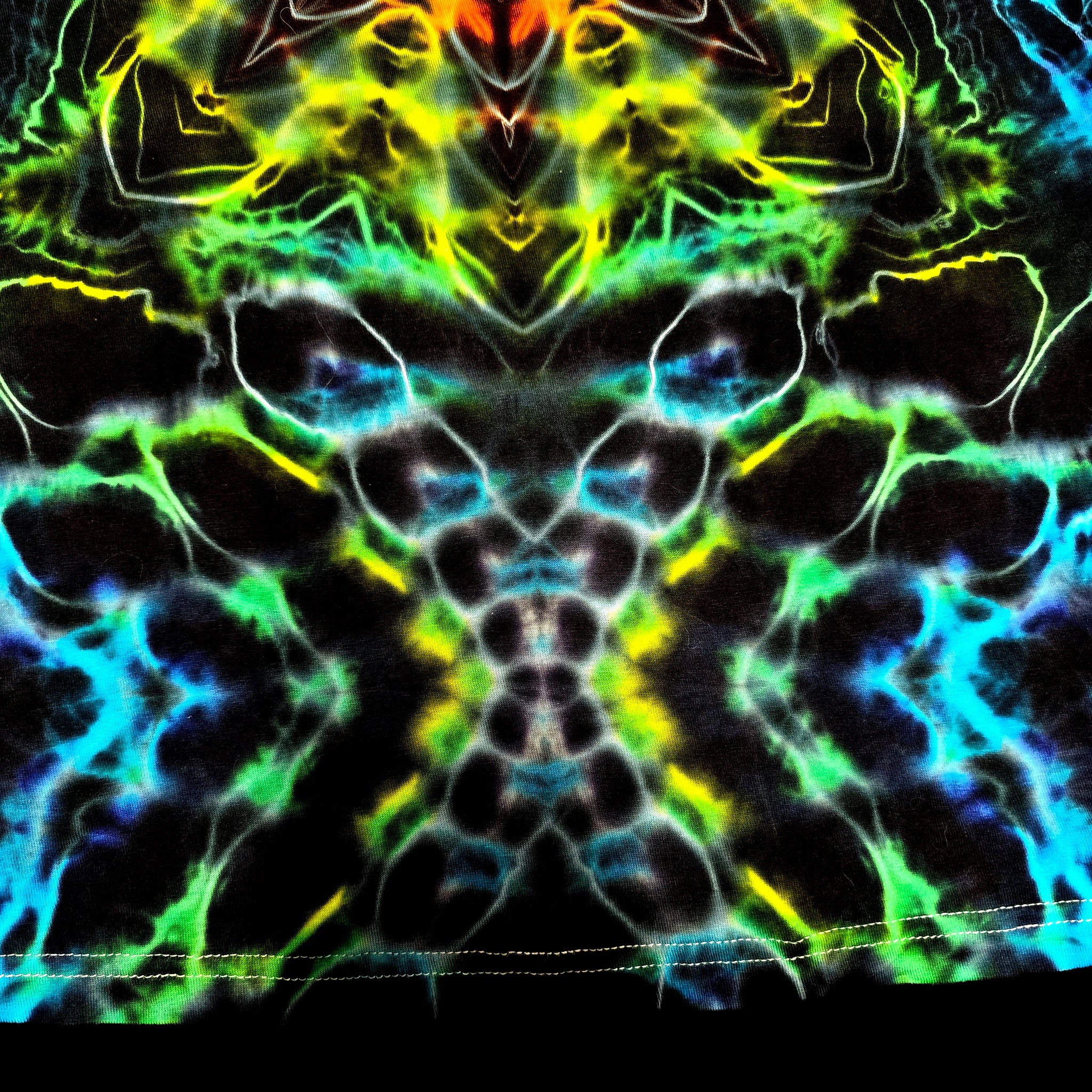 A close-up of a black fabric with a highly vibrant, symmetrical neon pattern featuring glowing green, blue, yellow, and orange veins on a black base.