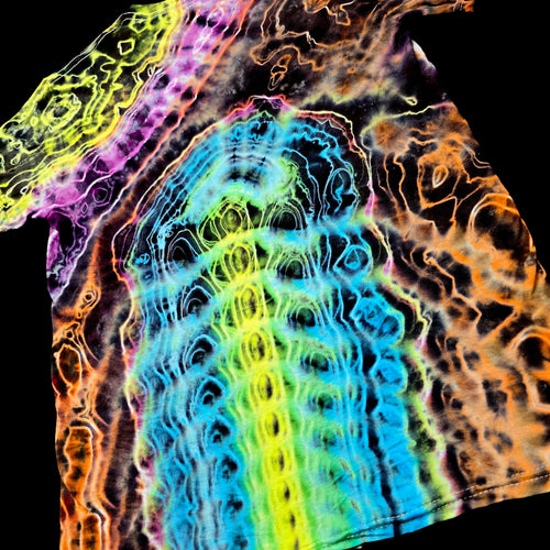 A close-up of a tie-dye or batik-printed fabric with a highly abstract, wavy pattern in multiple neon colors including blue, green, yellow, orange, pink, and purple on a black background.