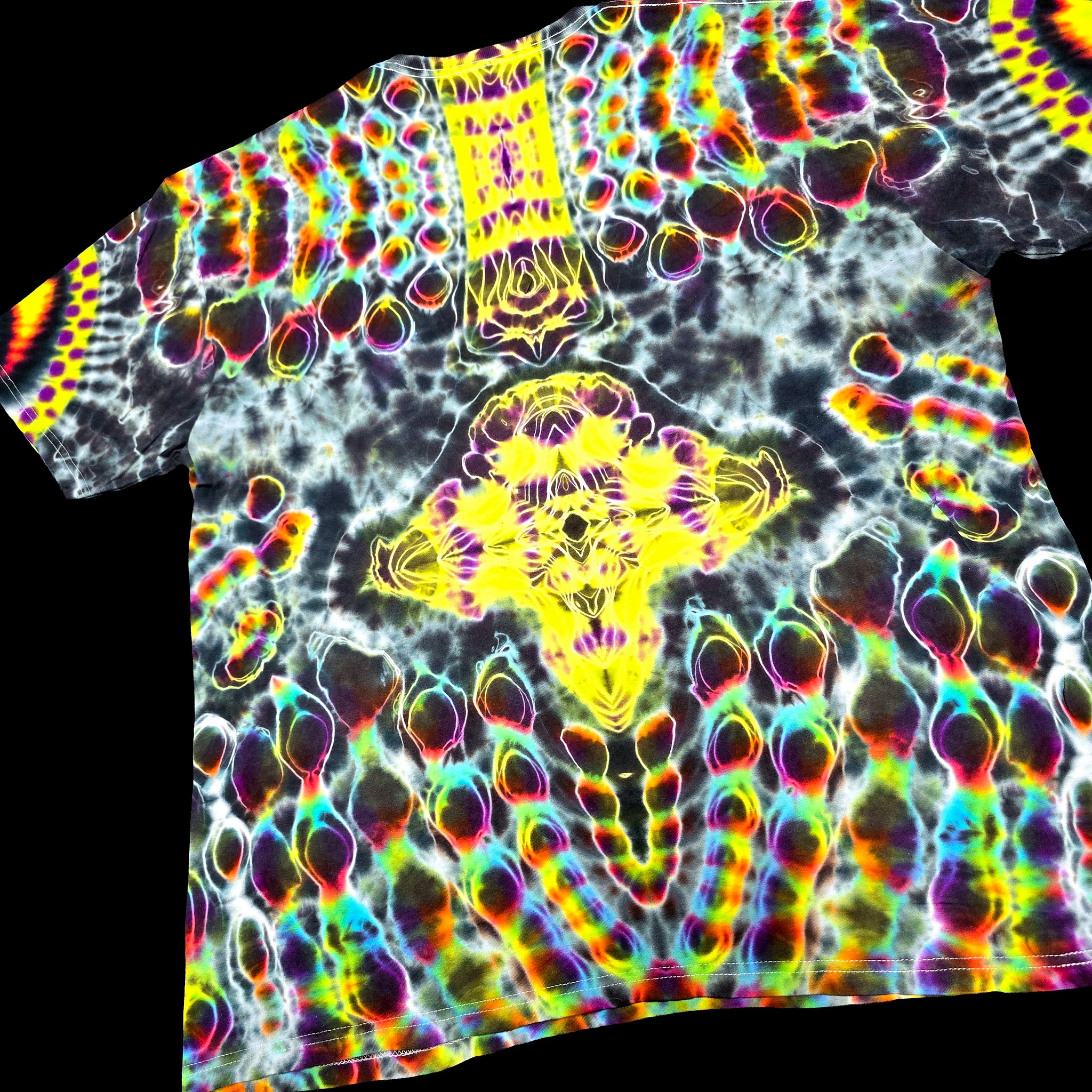 A short-sleeve t-shirt featuring a highly vibrant, psychedelic tie-dye pattern with neon yellow, pink, green, blue, and purple colors over a black and white base, shown against a solid black background.