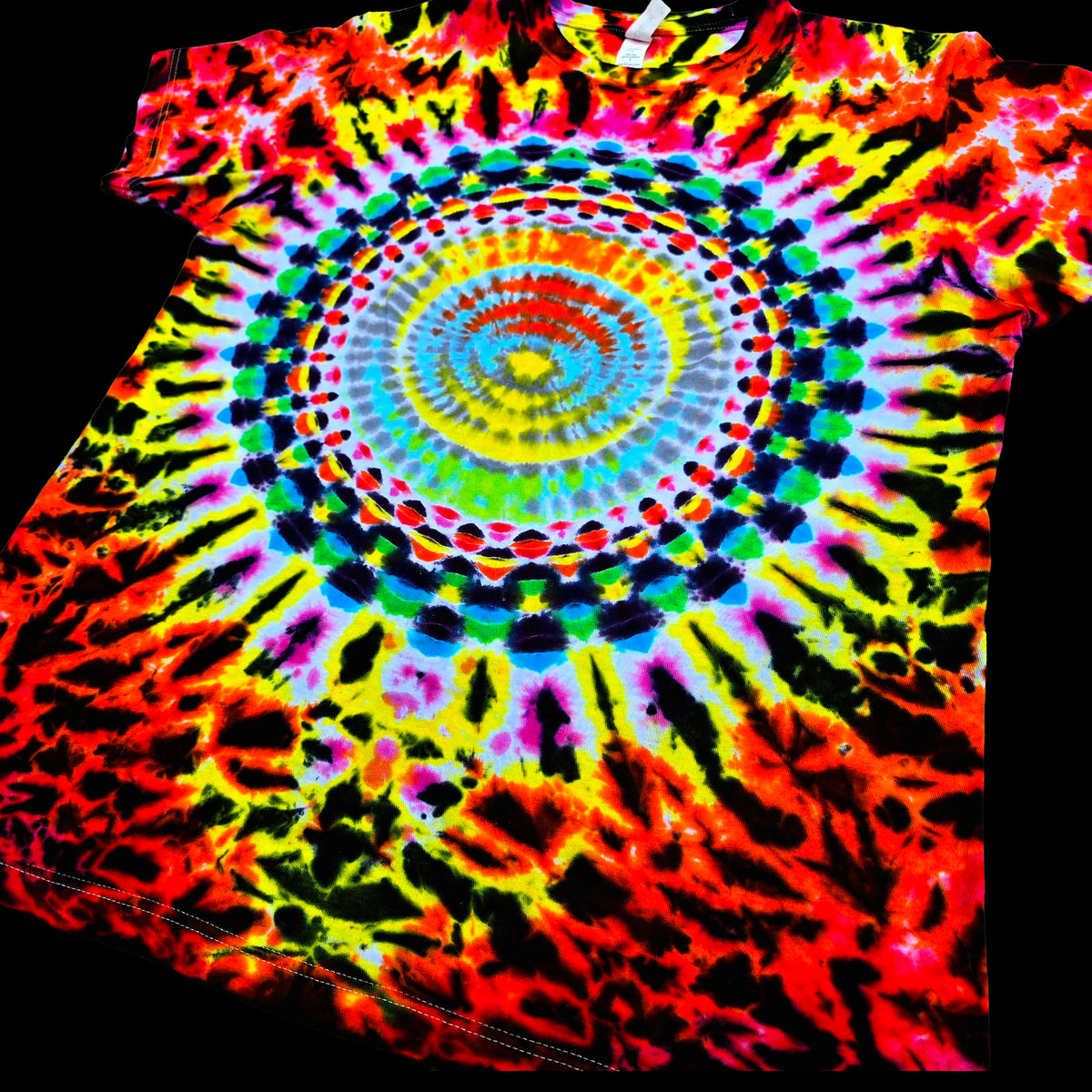 A short-sleeve tie-dye T-shirt with a large spiral mandala pattern in bright neon colors including red, orange, yellow, green, blue, purple, and black, shown against a black background.
