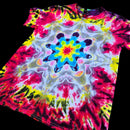 A short-sleeve tie-dye T-shirt laid flat on a black background, featuring a bright central mandala-style floral pattern with red, pink, yellow, blue, white, and black dye blends.