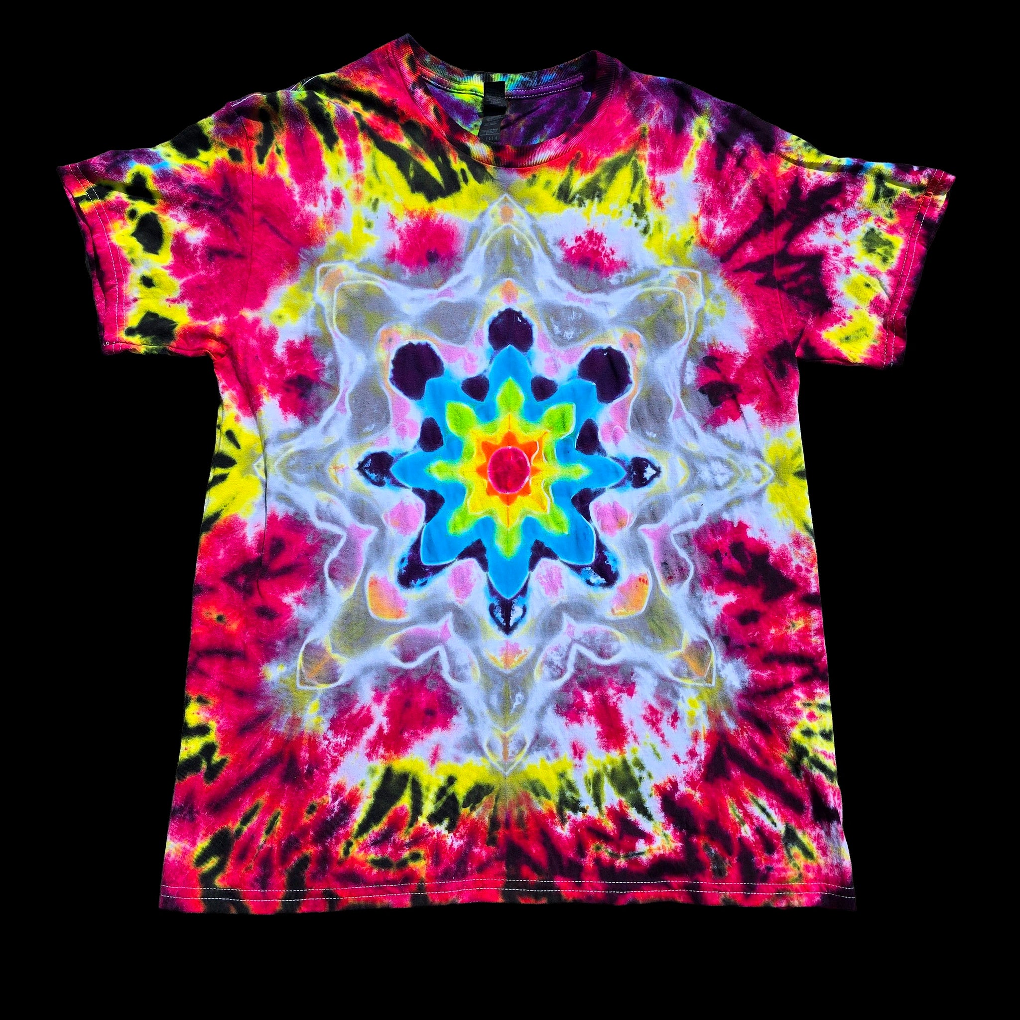 A short-sleeve crewneck tie-dye t-shirt featuring a vibrant, symmetrical kaleidoscopic mandala pattern in neon pink, yellow, blue, green, and white, displayed flat against a solid black background.