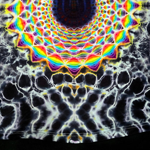 A close-up of a black fabric with a highly vibrant, symmetrical rainbow mandala pattern radiating from the top center, with a white and black marbled abstract pattern below.