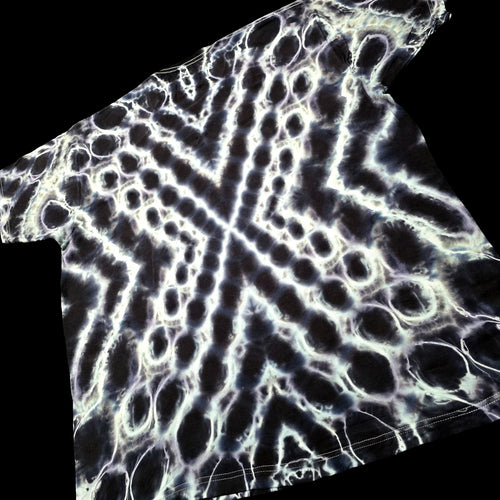 A short-sleeve t-shirt featuring a high-contrast black and white tie-dye pattern with a geometric, web-like design, shown against a solid black background.