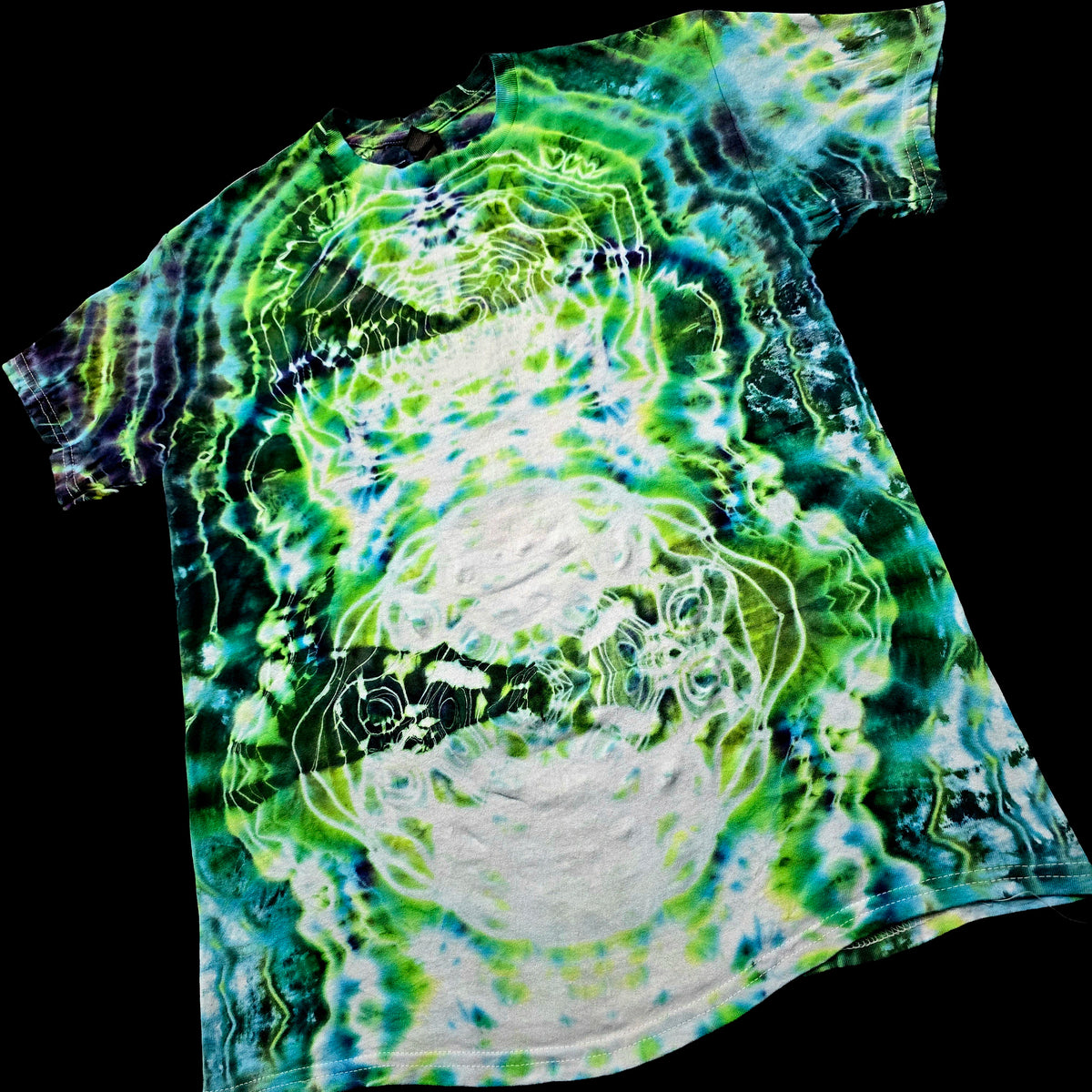 A short-sleeve t-shirt with a psychedelic tie-dye pattern in green, blue, and white, featuring a large white circular graphic in the center, shown against a solid black background.