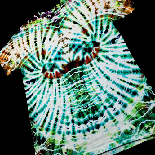 A close-up of a tie-dye garment featuring a spiral pattern in vibrant green, teal, white, and brown, set against a solid black background.