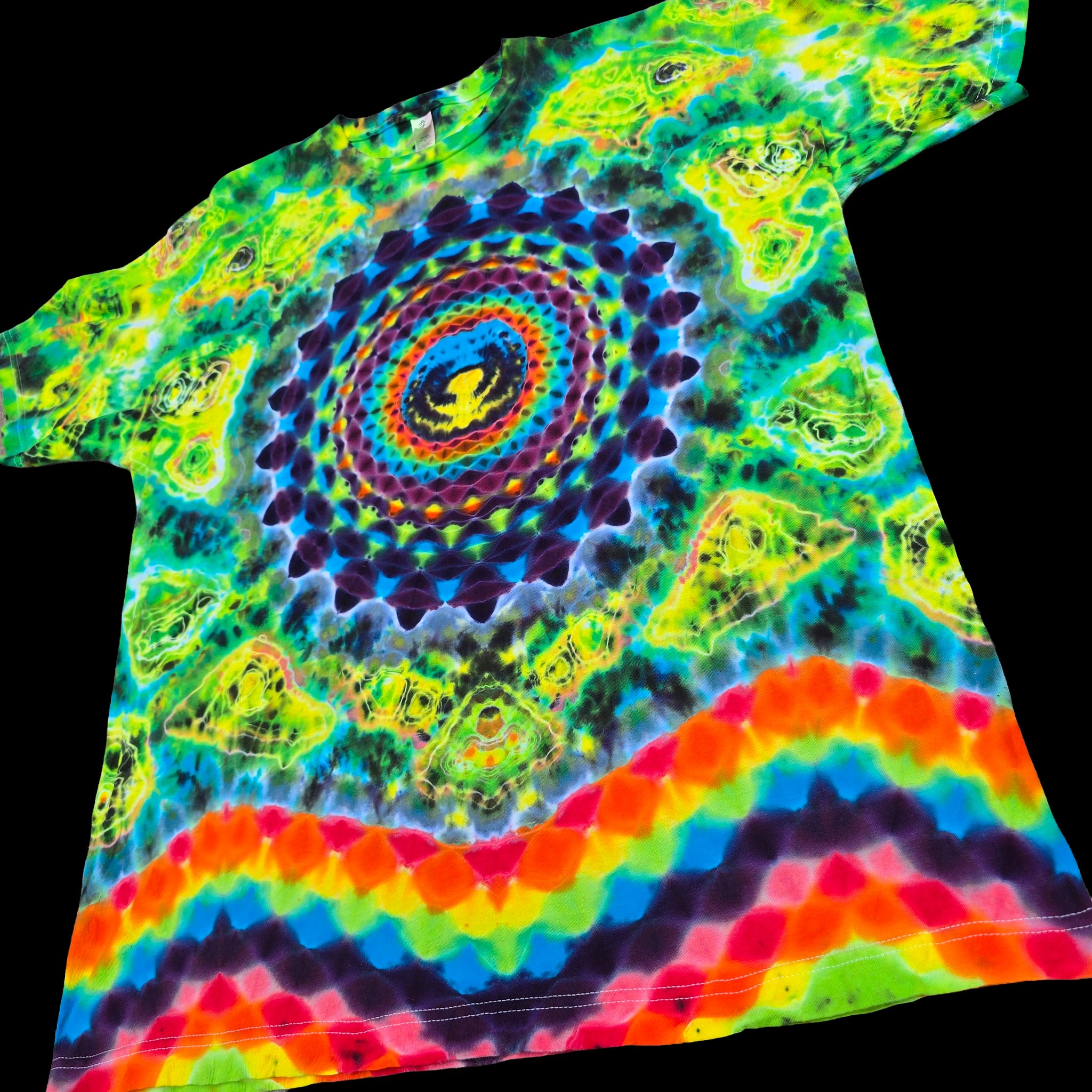 A short-sleeve tie-dye T-shirt laid flat on a black background, featuring a psychedelic mandala and eye pattern with rainbow stripes along the bottom hem.