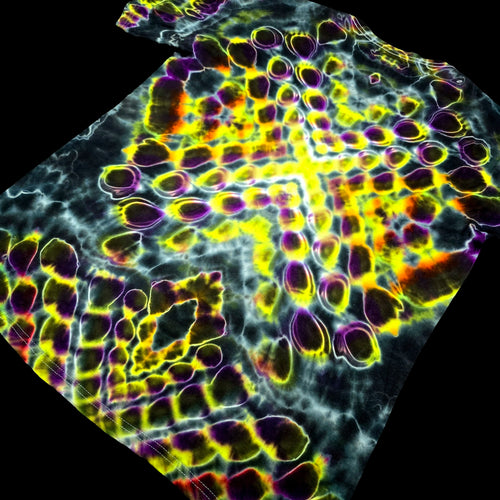 A close-up of a highly patterned fabric or material sample with an abstract organic design in bright yellow, purple, orange, and white over a dark background, shown against a black backdrop.