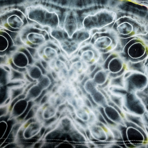 A close-up of a black and white patterned fabric with a symmetrical, organic cellular design and small yellow-green flecks.