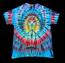 A short-sleeve tie-dye t-shirt with a vibrant spiral pattern in blue, red, yellow, green, and black, laid flat against a solid black background.