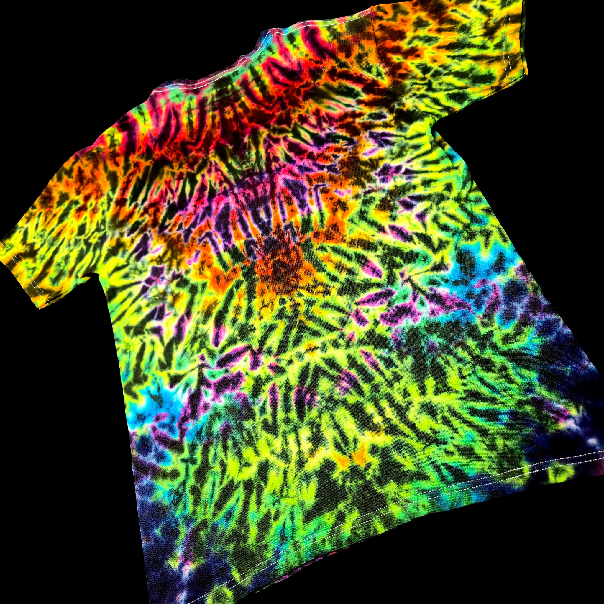 A short-sleeve tie-dye t-shirt with a vibrant spiral pattern of neon green, yellow, orange, pink, purple, and blue, displayed against a solid black background.