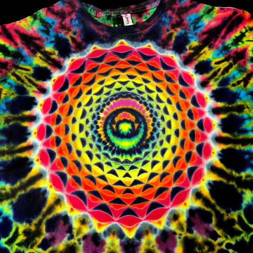 A close-up of a tie-dye t-shirt featuring a vibrant, symmetrical mandala pattern with concentric circles and geometric shapes in neon yellow, orange, red, pink, green, blue, and purple.