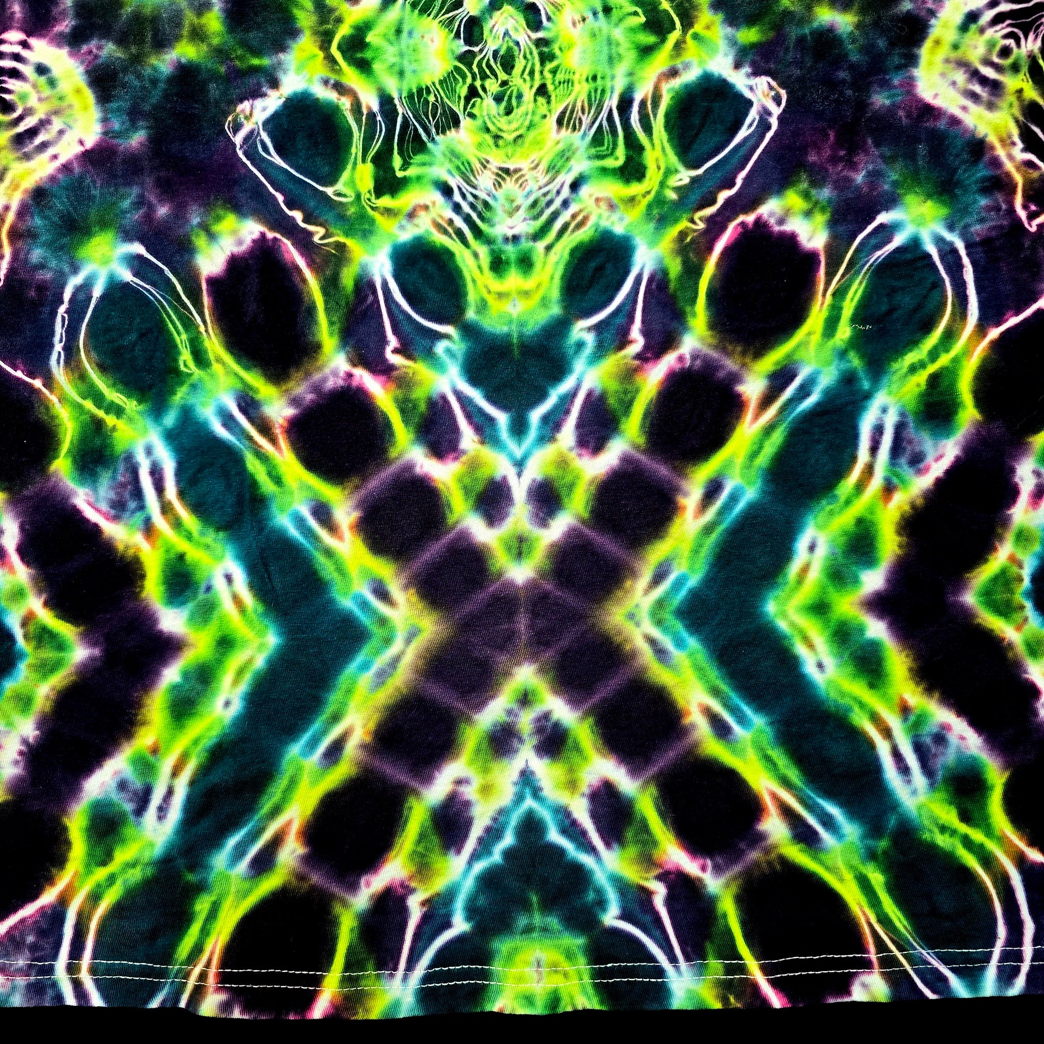 A close-up of a tie-dye fabric with a highly symmetrical, kaleidoscopic pattern featuring neon green, lime yellow, cyan, pink, and black.