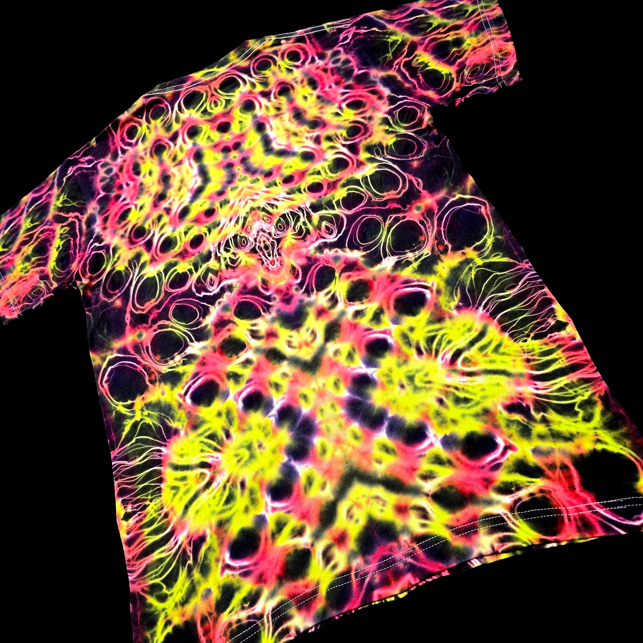 A short-sleeve crewneck t-shirt featuring a vibrant neon tie-dye pattern with bright yellow, pink, and purple swirls over a black base, shown against a solid black background.