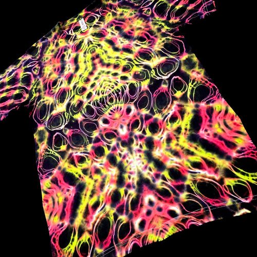 A short-sleeve tie-dye t-shirt with a vibrant neon pattern of pink, yellow, and green on a black background, shown against a solid black backdrop.