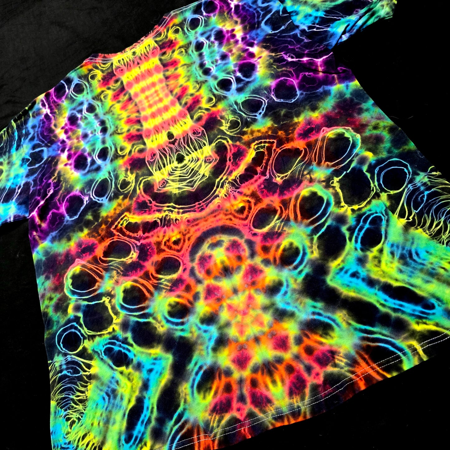 Angled back view showing layered fractal symmetry and flowing neon dye lines on Prism Core shirt
