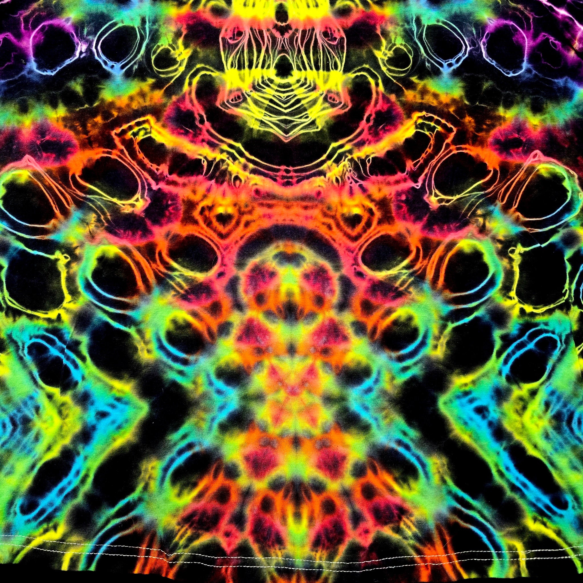 A vibrant, symmetrical tie-dye pattern with neon rainbow colors on a black background, featuring organic circular and wavy shapes.