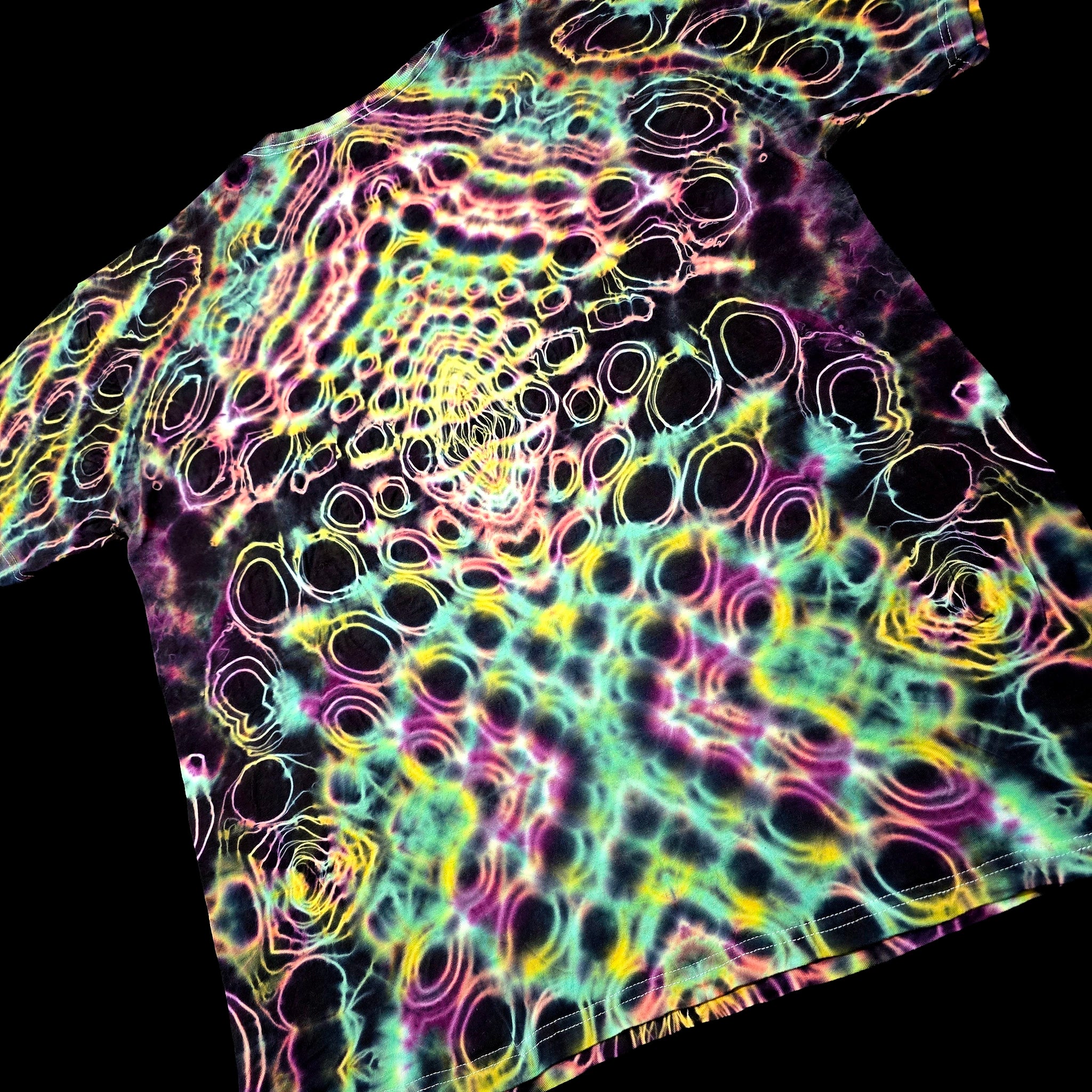 A short-sleeve t-shirt with a vibrant, psychedelic tie-dye pattern featuring concentric circles and wavy lines in neon pink, yellow, green, and purple over a black base, shown against a solid black background.