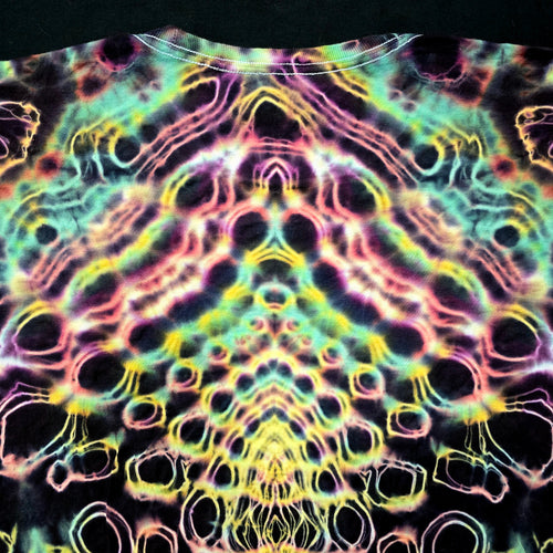 A close-up of a tie-dye t-shirt featuring a highly symmetrical, psychedelic pattern with neon pink, yellow, green, and blue outlines on a black base.