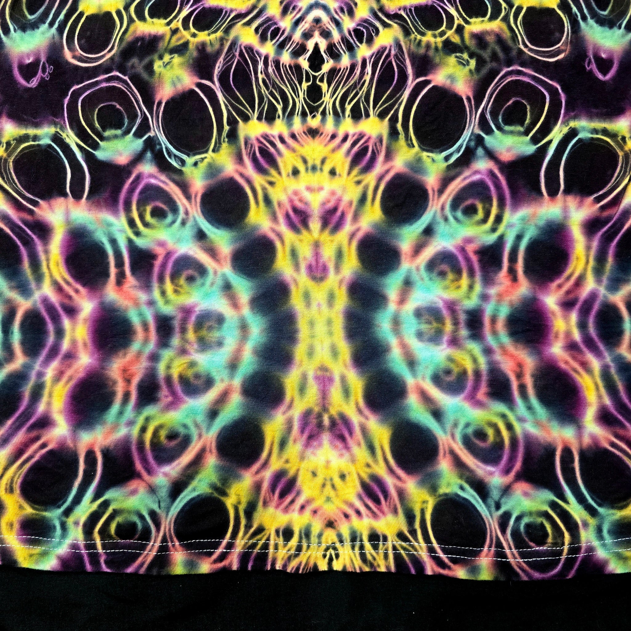 Close-up of front bottom tie-dye pattern featuring dense circular dye cells with neon outlines and dark negative space
